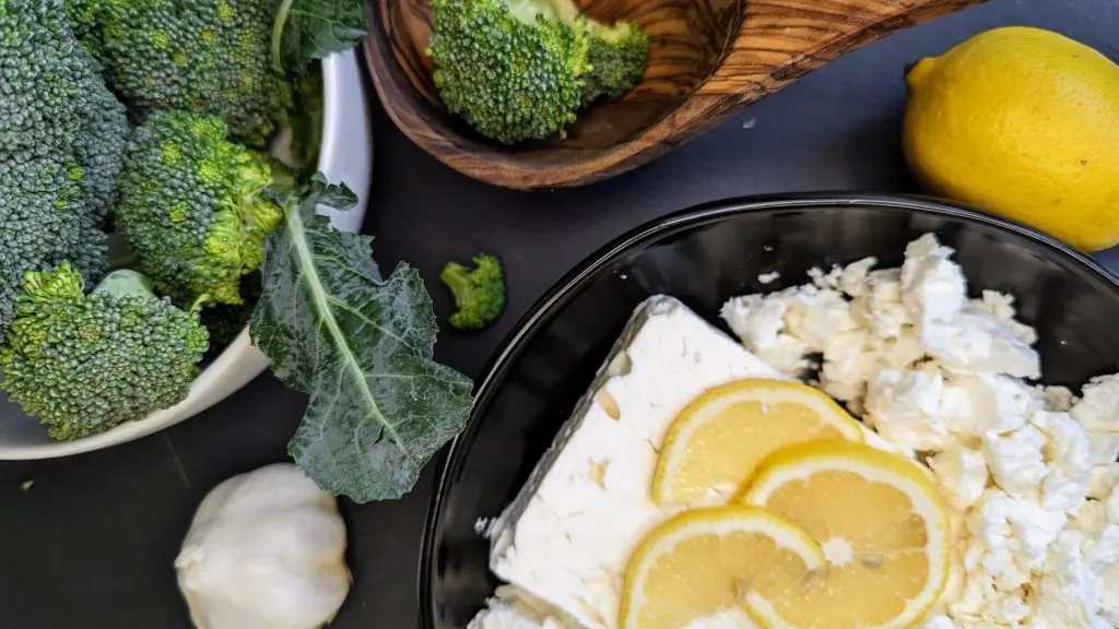 Ingredient flatlay for Broccoli Feta Soup, including broccoli, feta, lemon and garlic on a dark background